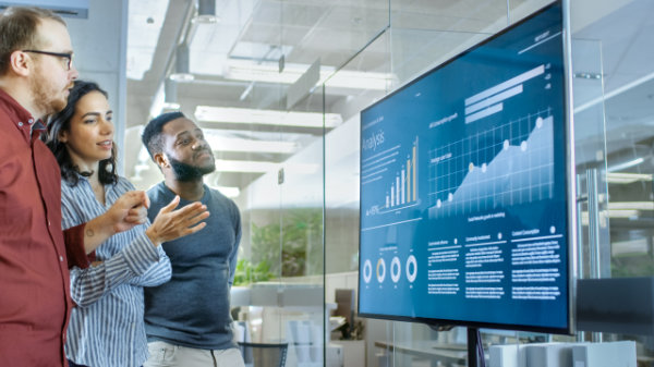 A group of employees looking at a digital screen chart showing an increase of company performance.